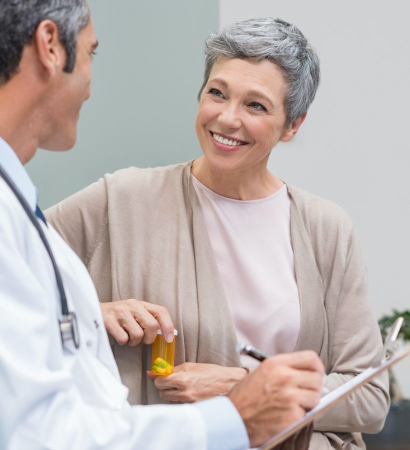 Senior doctor in conversation with senior woman holding medicine box. General practitioner and patient discussing at office. Happy doctor discussing with patient and prescribes pills.