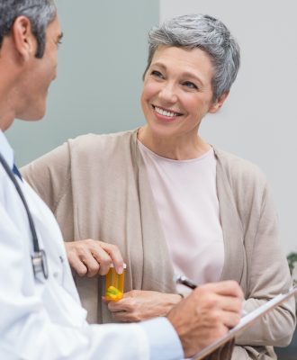 Senior doctor in conversation with senior woman holding medicine box. General practitioner and patient discussing at office. Happy doctor discussing with patient and prescribes pills.